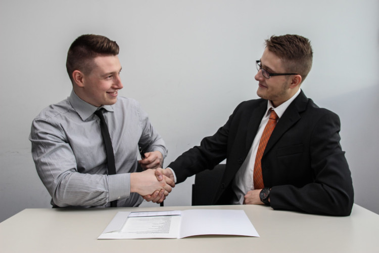 Two young men sitting at a table shake hands